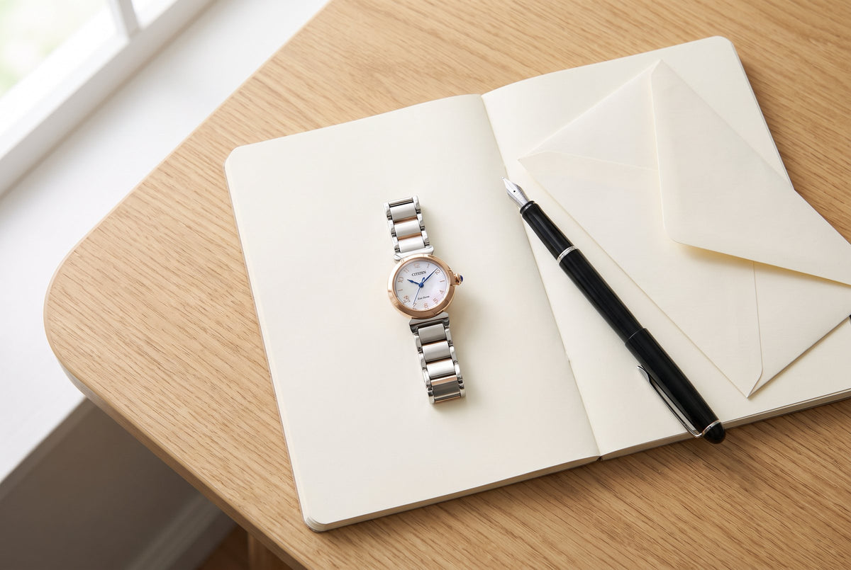 A Citizen L Mae watch on an open notebook beside a fountain pen and an envelope